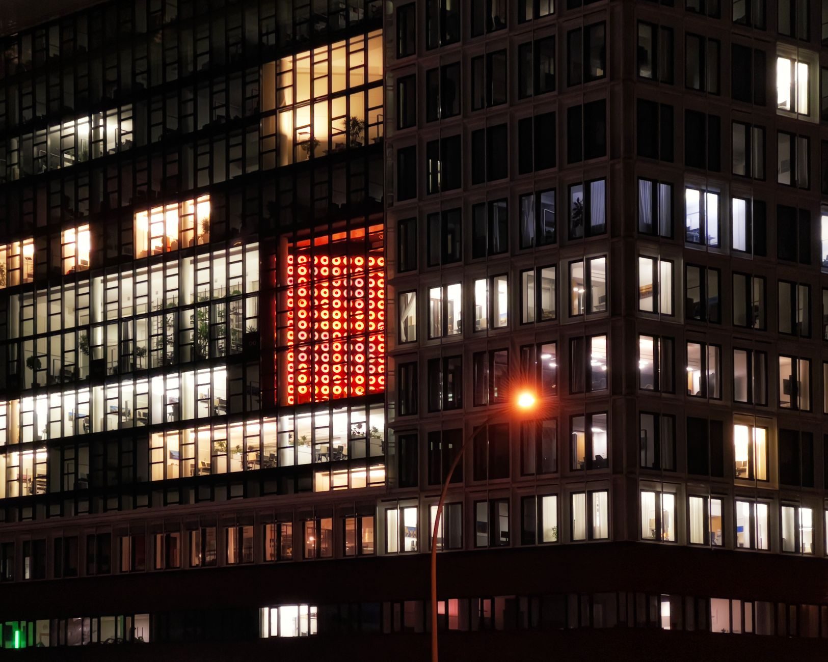 Night view of an urban building with illuminated windows and a distinctive red sign. Perfect for cityscape and architectural themes.
